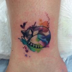 a cat tattoo on the ankle with watercolor paint splatters all over it