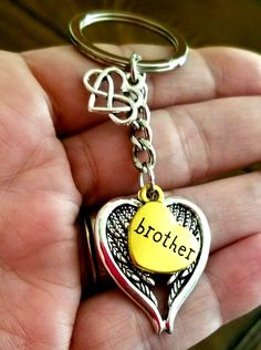 a hand holding a metal heart shaped keychain with the word brother written on it