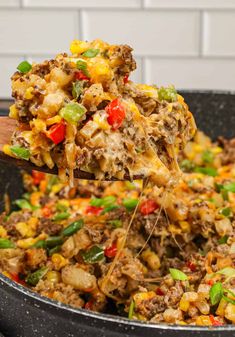 a wooden spoon full of food that is being lifted from a skillet to be eaten