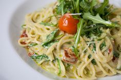 a white plate topped with pasta covered in sauce and veggies on top of it