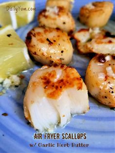 some scallops are sitting on a blue plate with lemon wedges next to them