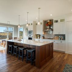 a large kitchen with an island in the middle and three bar stools at the end