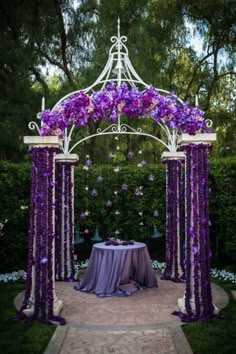 an outdoor wedding ceremony with purple flowers on the arch and table set up for it