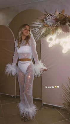 a woman standing in front of a mirror wearing a white outfit with feathers on it