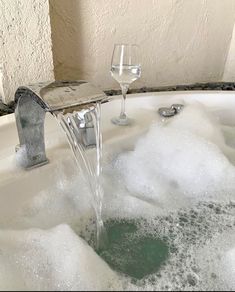 a wine glass is sitting in the bathtub with water running from it's faucet