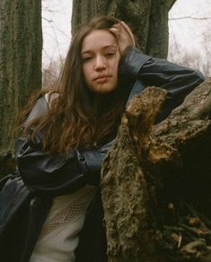 a woman standing next to a tree in the woods with her hands on her head