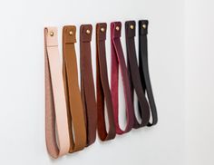 five different colored leather straps hanging on a wall