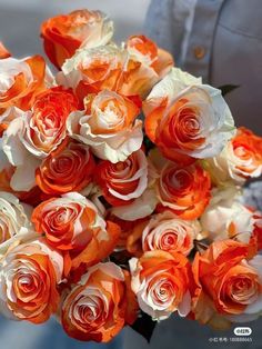 a bouquet of orange and white roses in someone's hand