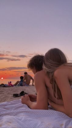 two people are sitting on the beach at sunset