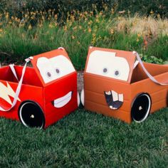 two cardboard cars are sitting in the grass, one is red and one is orange