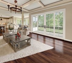 a large living room with wood floors and white walls, windows, and doors leading to a balcony