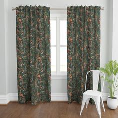 a white chair sitting next to a window covered in green and orange curtain panels on top of a hard wood floor