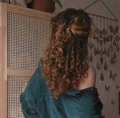 a woman with long curly hair standing in front of a wall and looking into the distance