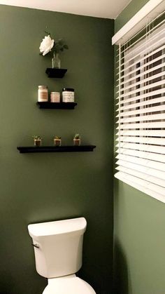 a white toilet sitting in a bathroom next to a window with blinds on the windowsill