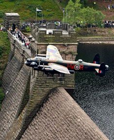 an airplane flying over a bridge with people standing on the side and looking at it