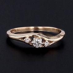 a gold ring with three diamond stones on the top and bottom, sitting on a black surface