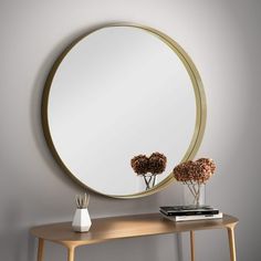 a round mirror sitting on top of a wooden table next to a vase with flowers