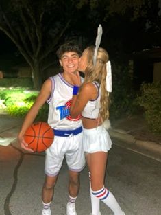 a man and woman dressed in cheerleader outfits standing next to each other holding a basketball