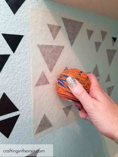 someone is holding an orange and black ball in front of a wall with triangles on it