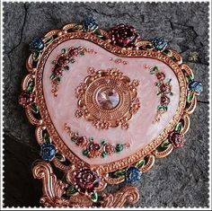 a pink heart shaped brooch sitting on top of a stone floor next to a rock