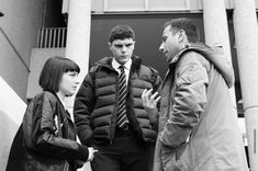 three people standing in front of a building talking to each other and one person wearing a tie