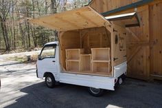 a small white truck parked in front of a wooden building with shelves on the back