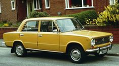 an old yellow car parked in front of a brick building