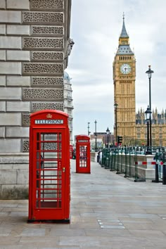 two red telephone booths sitting on the side of a street next to a clock tower