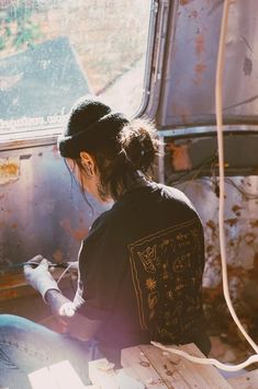 a woman sitting on top of a wooden bench next to an old bus window with graffiti all over it