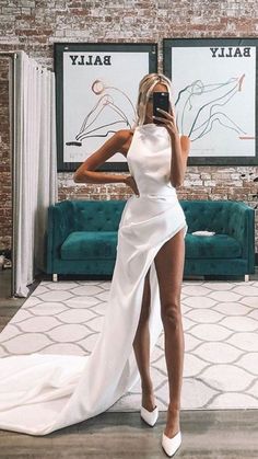 a woman in a white dress taking a selfie with her cell phone while wearing high heels