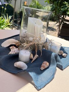 candles and seashells are placed in a glass vase on a blue towel with sea shells