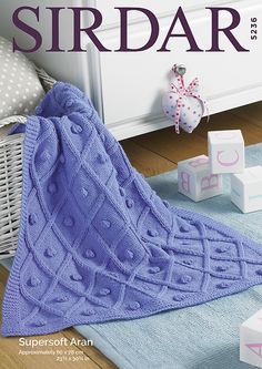 a knitted blanket sitting on top of a wooden floor next to boxes and toys