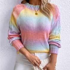 a woman wearing a rainbow colored sweater and white pants with her hand in her pocket