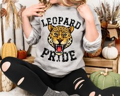 This is the perfect vintage school spirit sweatshirt! Leopard Pride! This distressed leopard sweatshirt is great for the sports moms and gift for high school sports fans! This retro distressed leopard is perfect on the popular Gildan brand sweatshirt. This vintage style sweatshirt will keep you warm throughout the sports season!  A pre-shrunk, classic fit sweater that's made with air-jet spun yarn for a soft feel and reduced pilling. ** P R O D U C T **  - 50% cotton, 50% polyester  - Pre-shrunk  - Classic fit  - Direct to Garment print (no stencils or vinyl which means it will last a lot longer)   - Printed and Shipped in the USA  - Due to different monitor screens colors may vary ** S I Z I N G **  - Consult size chart in listings for measurements  - Sizing is Unisex for all tees, runs t Leopard Shirt, High School Sports, School Spirit Shirts, Spirit Shirts, Vintage School, Branded Sweatshirts, Sports Mom, Mom Tees, Fitted Sweater