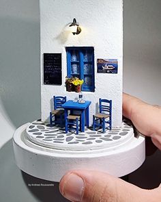 a hand holding a miniature model of a small table and chairs in front of a house