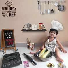 a little boy sitting on the floor in front of a pan filled with food and cooking utensils