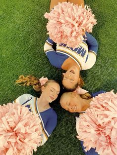 three cheerleaders laying on the ground with their pom poms around them