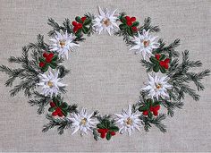 a christmas wreath made out of white flowers and green leaves on a gray background with red berries