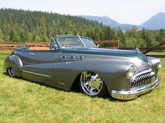 an old car parked in the grass with mountains in the background