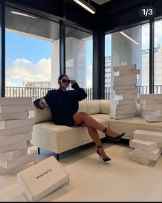 a woman sitting on top of a couch next to stacks of boxes and holding a drink