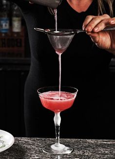 a woman pours a drink into a martini glass with a garnish on the rim