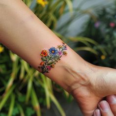 a person's arm with a flower tattoo on it and flowers in the background