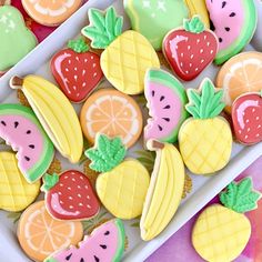 some decorated cookies are in a white box on a pink and yellow tablecloth with other colorful treats