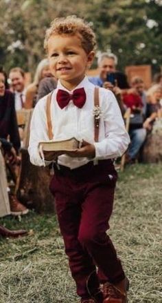 a little boy in a bow tie and suspenders walking down the aisle at a wedding