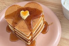 a stack of pancakes on a pink plate topped with syrup and a heart shaped butter