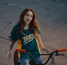 a woman riding a bike down a street next to a parking lot with her hand on the handlebars