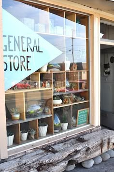 a store front window that has plants in the windows and on display behind it is a wooden bench