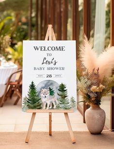 a welcome sign for a baby shower with a white dog and pine trees in the background