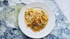 a white plate topped with pasta and sauce on top of a marble countertop next to a fork