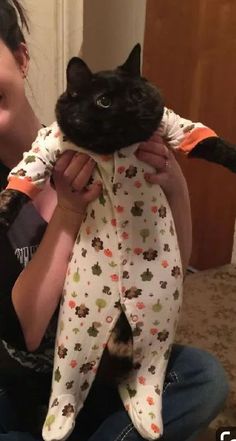 a woman holding a black cat in her arms and wearing pajamas on it's back